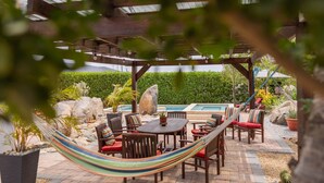 An outdoor patio with a pool, wooden furniture, and a hammock. - Oasis of Relaxation 1BR Apartment w/pool -Sunrise (Noord)