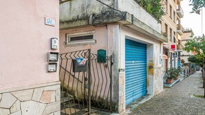 Uma rua de paralelepípedos estreita com um edifício rosa, uma porta de garagem azul e um portão de metal.