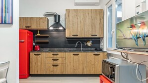 Uma cozinha compacta com armários de madeira, uma geladeira vermelha, micro-ondas e torradeira sobre uma mesa vermelha.