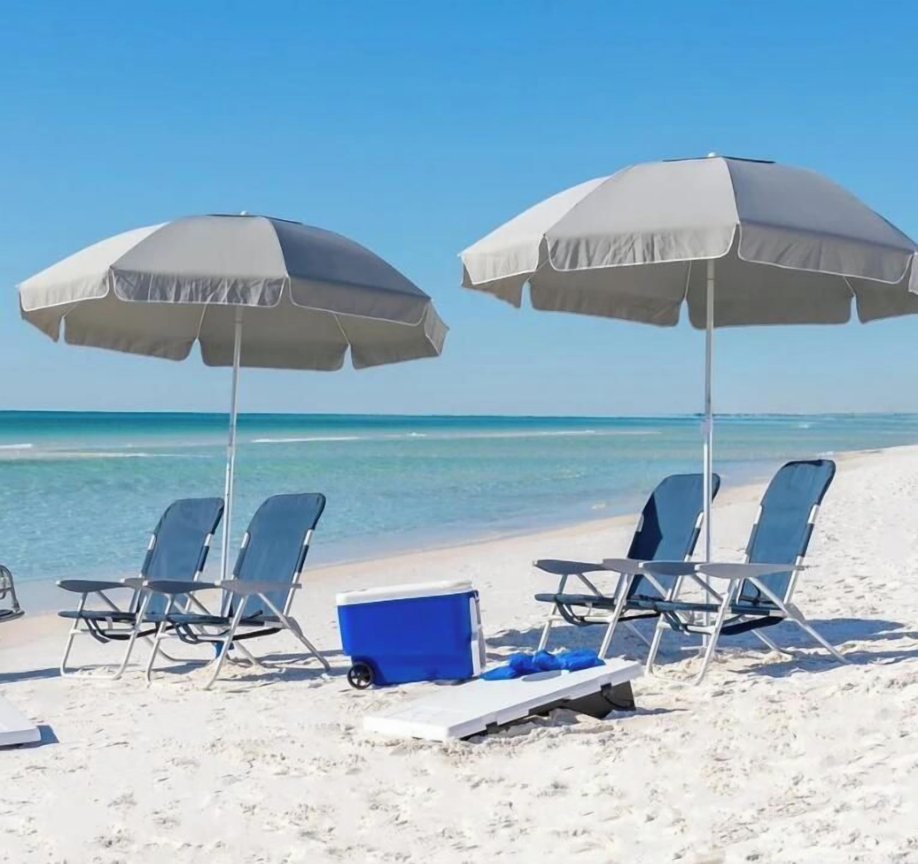A beach with two umbrellas, four lounge chairs, and a cooler on the sand.