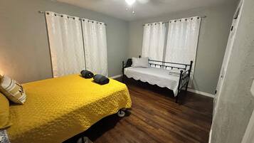 A bedroom with a yellow bedspread, two rolled towels, a white bed with a white bedspread, and a ceiling fan.