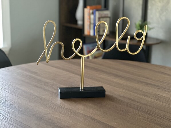 A gold "hello" sign on a black base, placed on a wooden table.