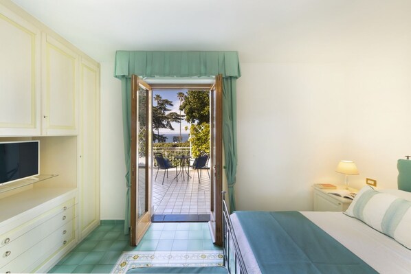 Un dormitorio con cama, televisor, mesita de noche y vista a un patio exterior con sillas y una mesa.