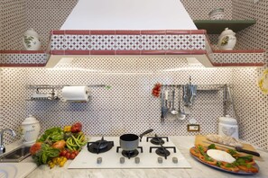 A kitchen with patterned backsplash, a gas stove, a sink, and various kitchen utensils.