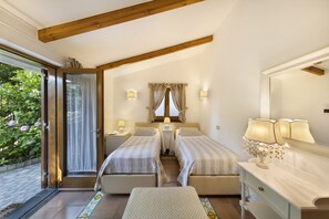 Un dormitorio con dos camas, una mesita de noche con lámparas, una ventana con cortinas y una puerta que da a un jardín.