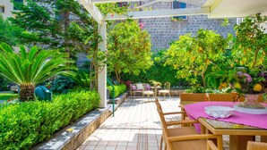 Un patio con pérgola, mobiliario exterior y abundante vegetación.