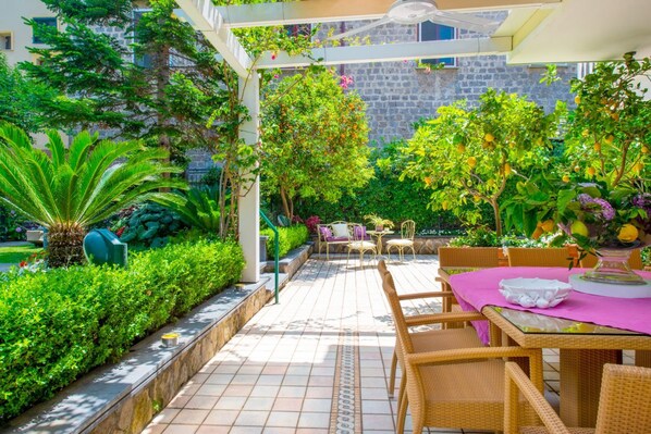 Un patio con pérgola, mobiliario exterior y abundante vegetación.