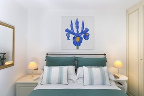Camera d'albergo ordinata con un letto, due comodini, una lampada a parete, un'opera d'arte incorniciata e uno specchio.