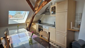 A kitchen with wooden beams, a skylight, a dining table with a vase, and tiled flooring. - Ferienwohnung Jesus - Großzügiges Loft mit Blick auf Burg und Kirchturm (Kevelaer)