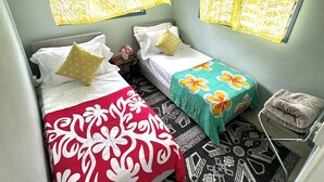 Een kleine, goed verlichte kamer met twee enkele bedden, een plafondventilator en decoratieve gordijnen.