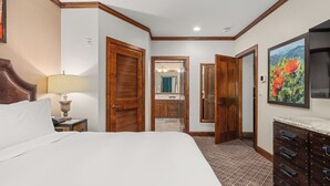 Habitación de hotel con una cama grande, un aparador, un espejo y un baño visible a través de una puerta abierta.