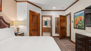 Habitación de hotel con una cama grande, puertas de madera, un baño visible a través de una puerta abierta y un aparador con cajones.
