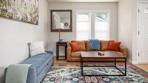 A living room with a blue sofa, a brown leather couch, a coffee table, and a patterned rug. - Bay Breeze Getaway | Blocks to the Beach | Downtown | AC | Fenced Yard (Traverse City)