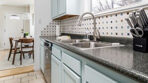 A modern kitchen with light blue cabinets, a granite countertop, and a window with lace curtains. - Bay Breeze Getaway | Blocks to the Beach | Downtown | AC | Fenced Yard (Traverse City)