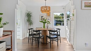 A dining area with a round table, black chairs, a hanging light fixture, and a view of the outdoors through a window. - Charming Urban Bungalow with Garden and Deck (Santa Barbara)