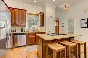 A kitchen with wooden cabinets, stainless steel appliances, a large island with bar stools, and a window with blinds.
