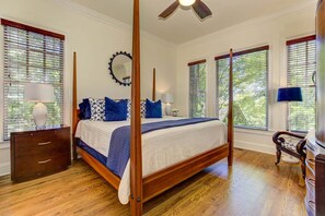 Un lit à baldaquin avec une couvre-lit blanche et bleue, une tête de lit en bois et des tables de chevet assorties, chacune surmontée d’une lampe.