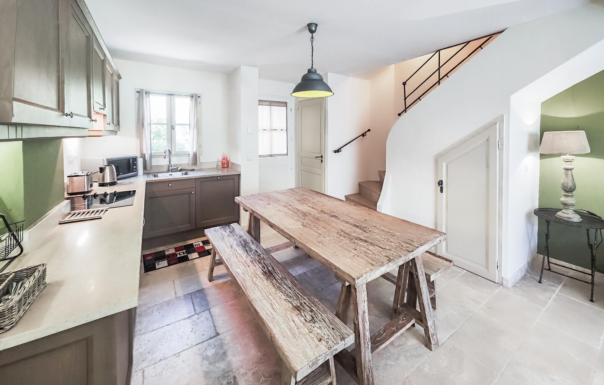 A modern kitchen with a wooden table and bench, a staircase, and a dining area.