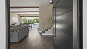 Um interior moderno com sofá cinzento, piso de madeira, escada e área de refeições com assentos externos.