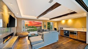 Uma sala de estar moderna com lareira, sofá seccional e área de cozinha com armários de madeira.