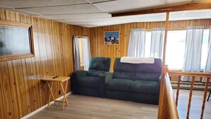 Una habitación acogedora con paneles de madera, un sofá verde oscuro, una pequeña mesa de madera y un cuadro de un alce en la pared.