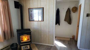 Una habitación con estufa de leña, un cuadro enmarcado en la pared y una puerta que da a otra estancia.