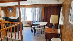 Un acogedor interior de cabaña con una escalera de madera, un comedor con mesa y sillas, un sofá y una lámpara.