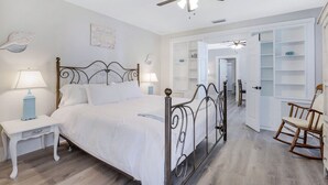 A bedroom with a bed, two bedside tables, a ceiling fan, a rocking chair, and a white wardrobe. - Urban Tropical Fort Myers Retreat in Historic Downtown River District (Fort Myers)