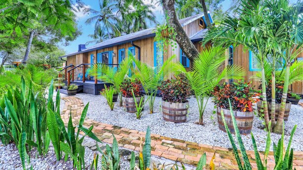 A wooden house with blue accents, surrounded by lush tropical plants and a gravel pathway. - Urban Tropical Fort Myers Retreat in Historic Downtown River District (Fort Myers)
