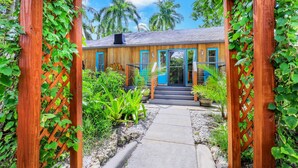 A wooden house with a porch, surrounded by lush greenery and palm trees. - Urban Tropical Fort Myers Retreat in Historic Downtown River District (Fort Myers)