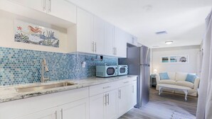 A modern kitchen with white cabinets, a blue mosaic backsplash, and a stainless steel refrigerator. - Urban Tropical Fort Myers Retreat in Historic Downtown River District (Fort Myers)