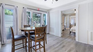 A dining area with a wooden table and chairs, a ceiling fan, and a view through large windows. - Urban Tropical Fort Myers Retreat in Historic Downtown River District (Fort Myers)