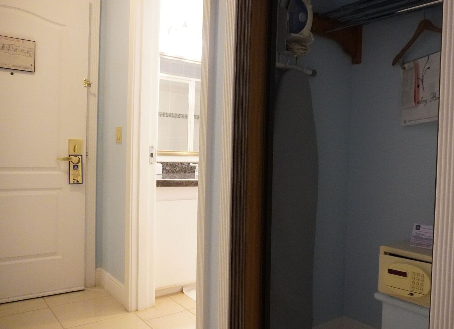 A hotel room with a white door, a bathroom with a towel rack, and a small window.