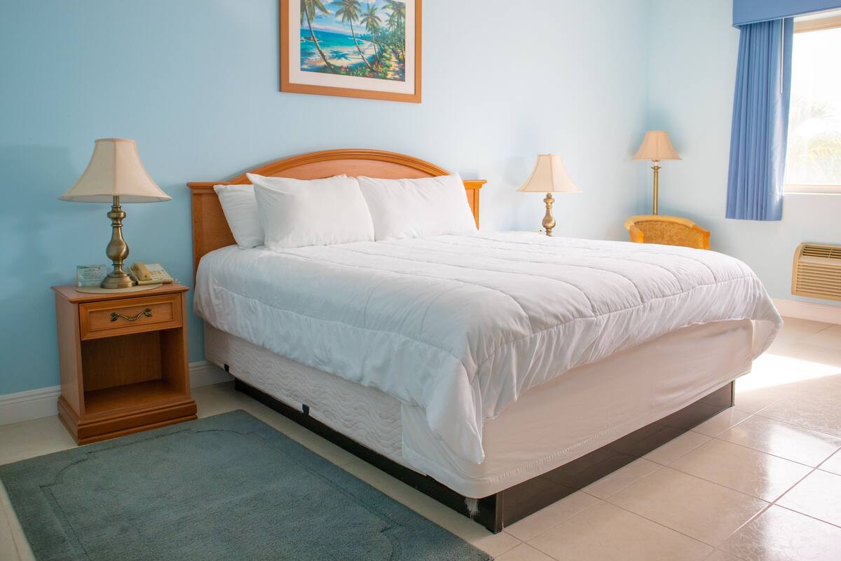 A neatly arranged bedroom with a bed, bedside tables, lamps, a painting, and a window with curtains.