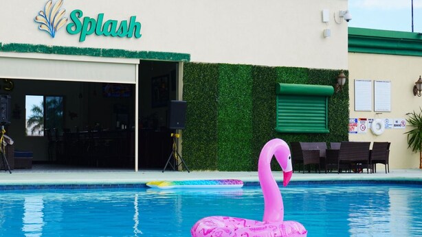 A swimming pool with a pink flamingo float, a 'Splash' sign, and a green hedge. - Princess Vegas Hotel & Casino (Corozal)