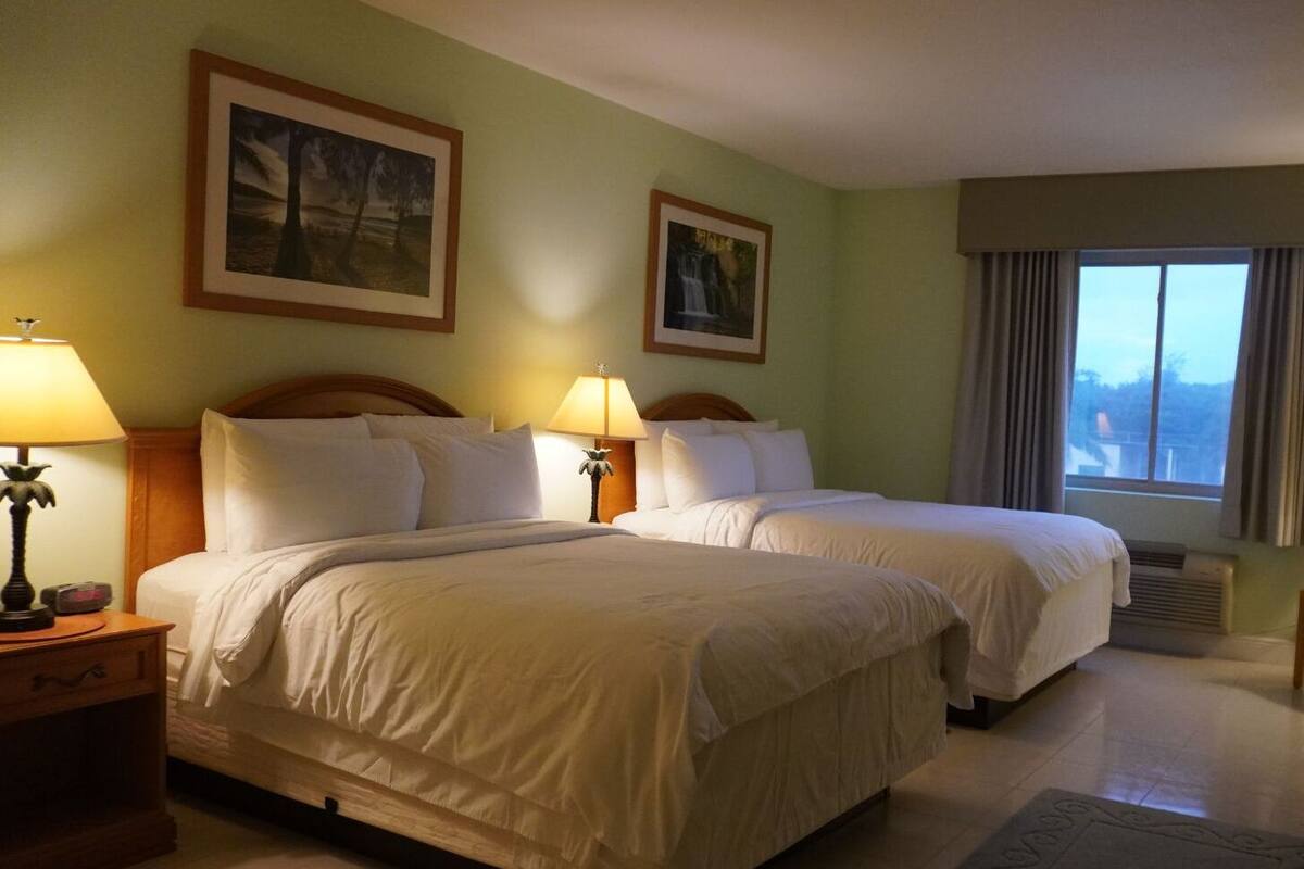 A hotel room with two beds, a nightstand with a lamp, and two framed pictures on the wall.