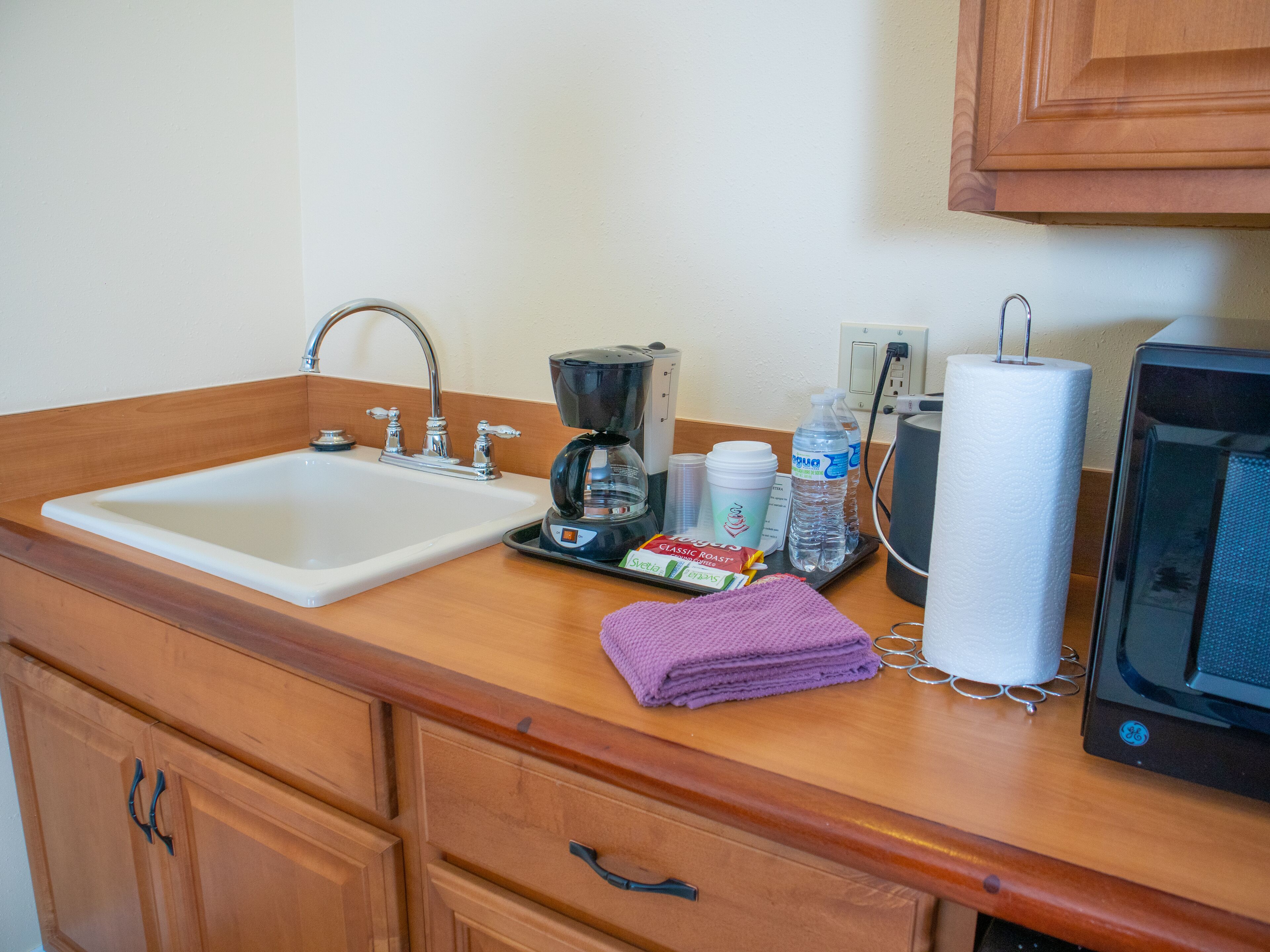 A kitchen with a sink, coffee maker, water bottle, and a paper towel dispenser.