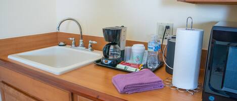 A kitchen with a sink, coffee maker, water bottle, and a paper towel dispenser.