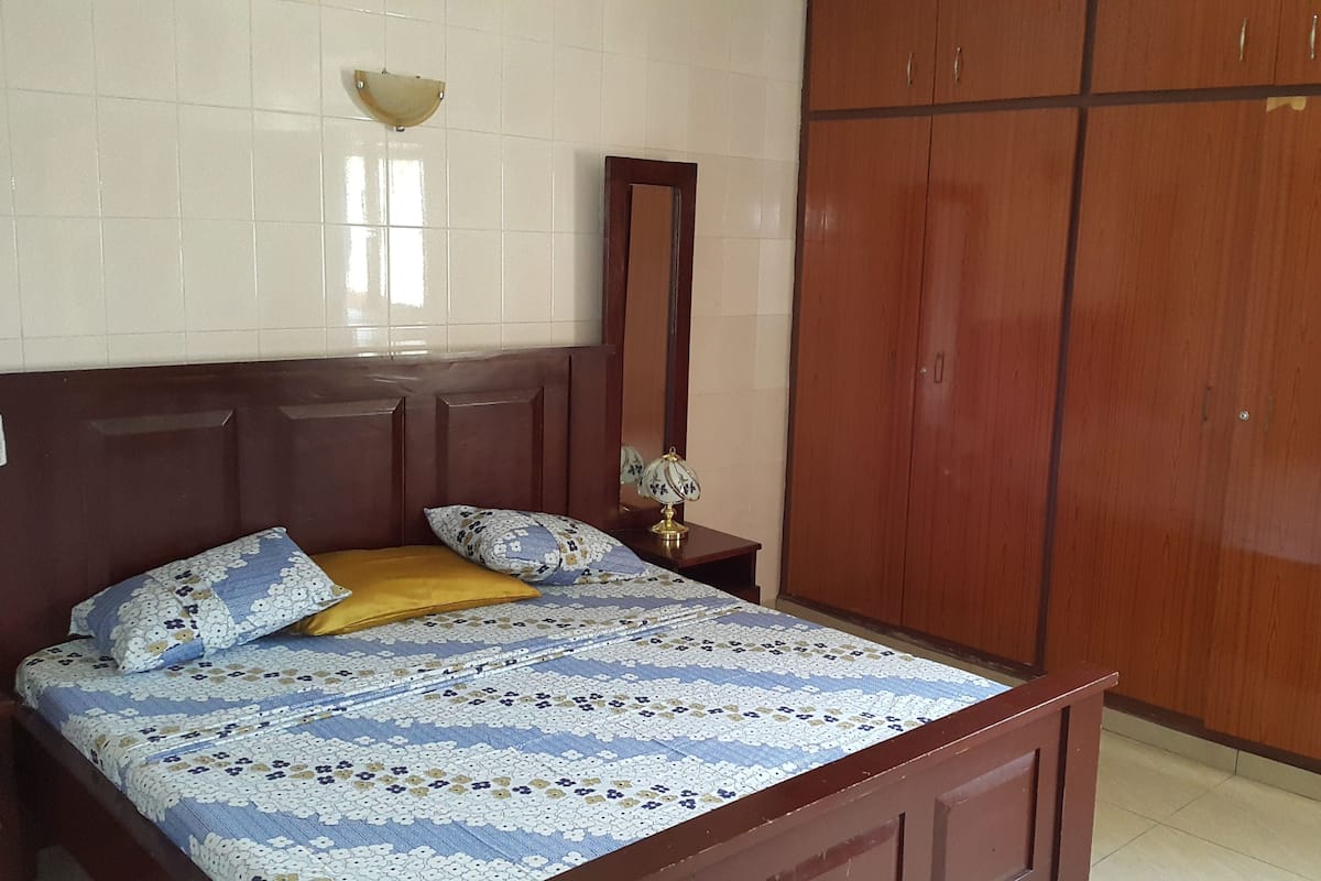 Ein Schlafzimmer mit Bett, Holzschrank und Nachttisch mit Lampe.