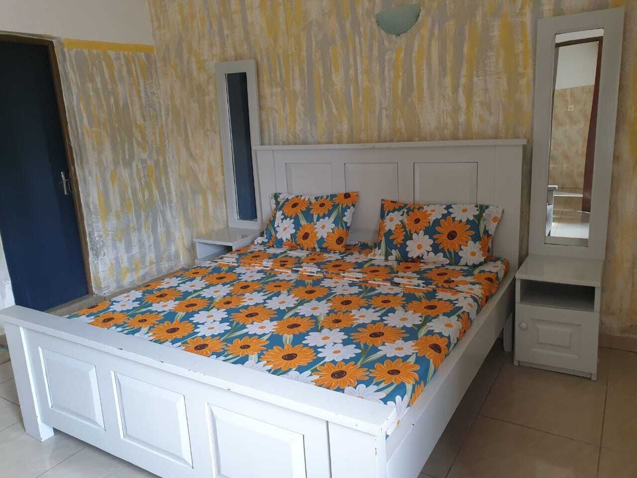 A bed with a floral bedspread, a bedside table, a nightstand, and a mirror.