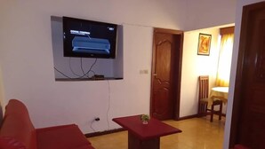 A living room with red sofas, a small table with a plant, and a TV mounted on the wall displaying 'SIGNAL CONTINUOUS'. - Hotel Résidence Georges Colette Abidjan  (Abidjan)