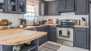 A modern kitchen with dark cabinets, a wooden countertop, stainless steel appliances, and a window providing natural light.