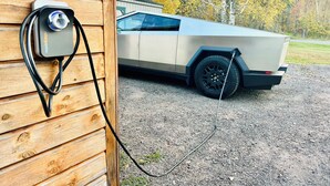 A vehicle parked outside a wooden building with a charging station attached to the wall.