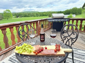 Eine Holzterrasse mit einem Tisch, der für eine Mahlzeit gedeckt ist, darunter eine Platte mit Wurstwaren, Weingläser und eine Weinflasche.