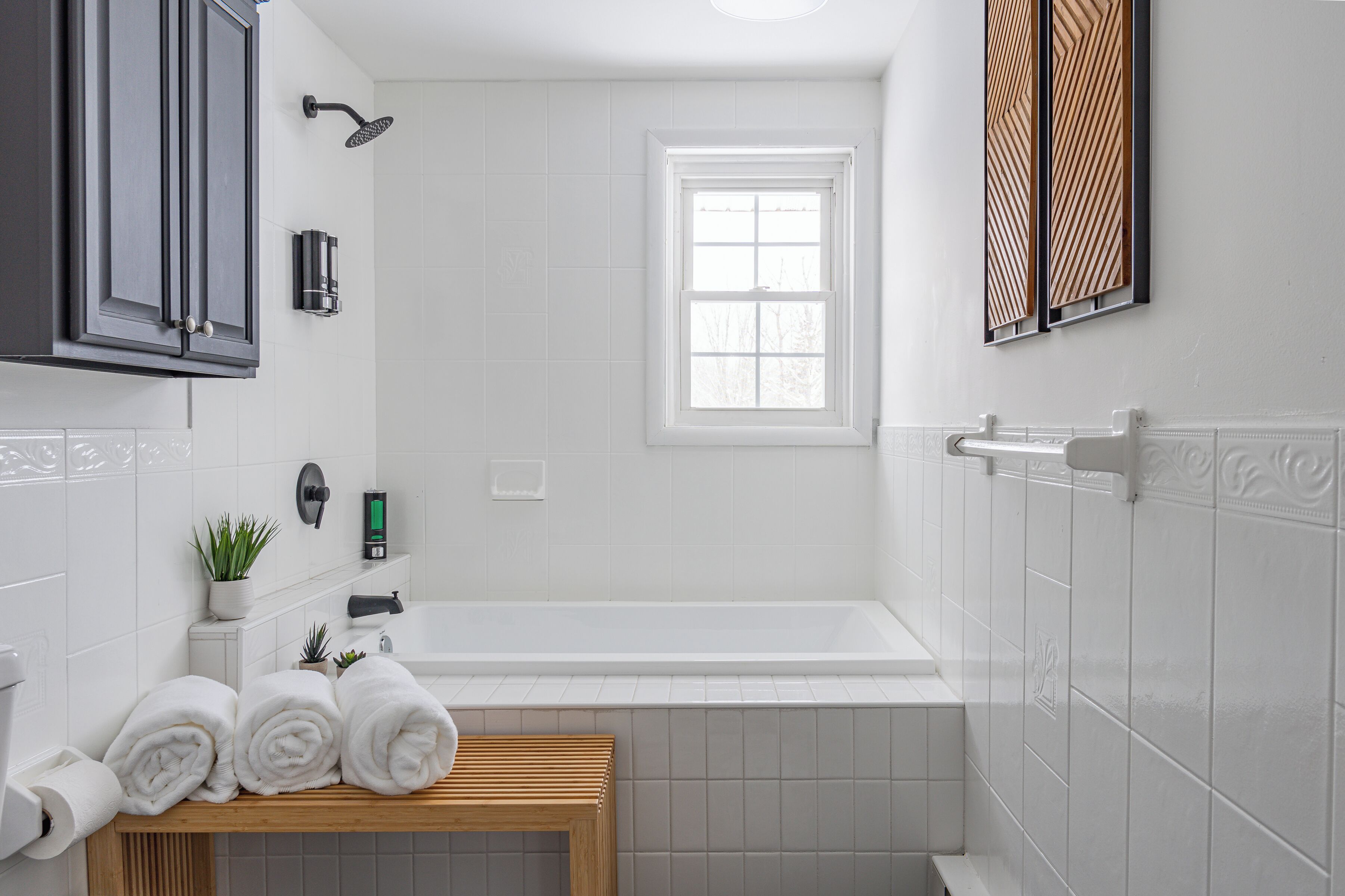 A modern bathroom with a bathtub, a window, and a wooden bench.