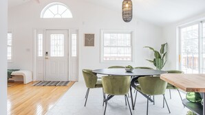 A dining area with a round table and six chairs, a ceiling fan, and a large window with a view of trees.