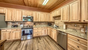 Una cocina con armarios de madera, encimeras de granito, electrodomésticos de acero inoxidable y techo de madera con iluminación fluorescente.
