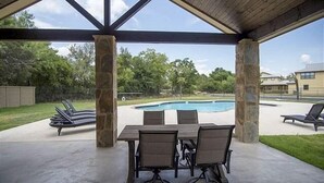 Un patio al aire libre con piscina, pilares de piedra y sillones de descanso.