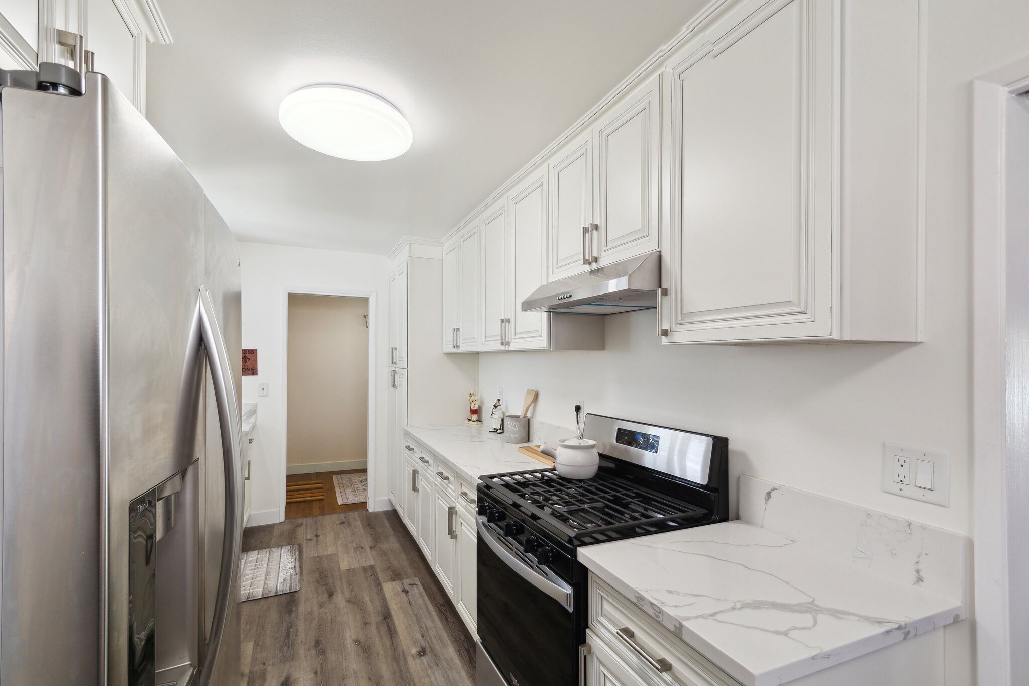 A compact kitchen with white cabinets, a stainless steel refrigerator, a black stove, and a marble countertop.