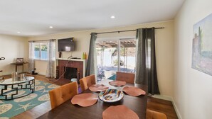 A spacious living room with a wooden dining table, comfortable seating, a fireplace, and a large window with curtains. - Modern Relaxing Retreat With Private Pool 4 Bedroom Home by RedAwning (Azusa)